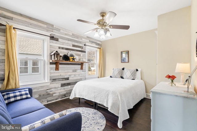 bedroom featuring wood walls, dark wood-style floors, and a ceiling fan