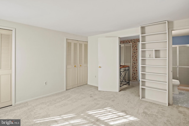 unfurnished bedroom with ensuite bath, multiple closets, and light colored carpet