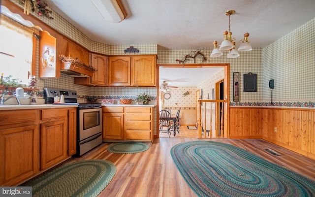 kitchen featuring ceiling fan with notable chandelier, pendant lighting, stainless steel electric stove, and light hardwood / wood-style flooring