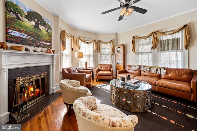 living area with crown molding, a glass covered fireplace, wood-type flooring, and ceiling fan