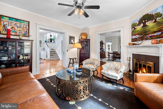 living area with stairs, wood finished floors, a glass covered fireplace, and ornamental molding