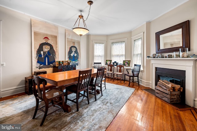 dining room with crown molding, hardwood / wood-style floors, a glass covered fireplace, and baseboards