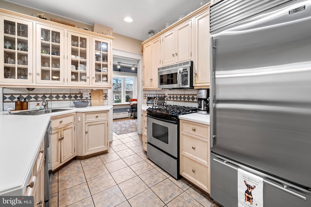 kitchen with light tile patterned floors, backsplash, cream cabinets, stainless steel appliances, and a sink