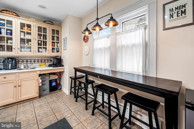 kitchen featuring light tile patterned floors, light countertops, decorative backsplash, glass insert cabinets, and a sink