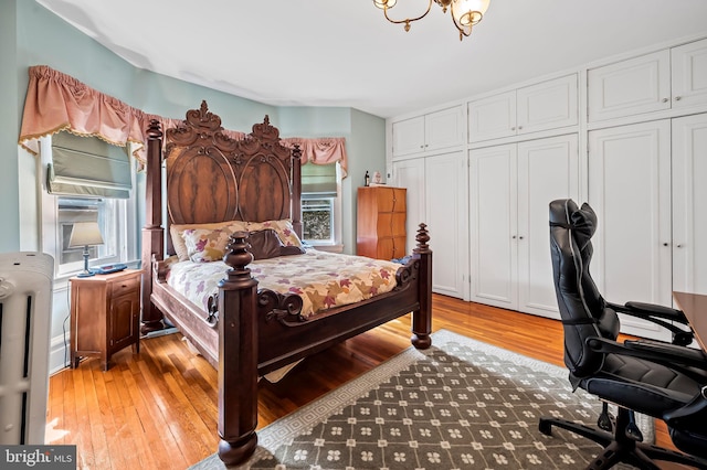 bedroom featuring light wood finished floors, radiator heating unit, and multiple closets