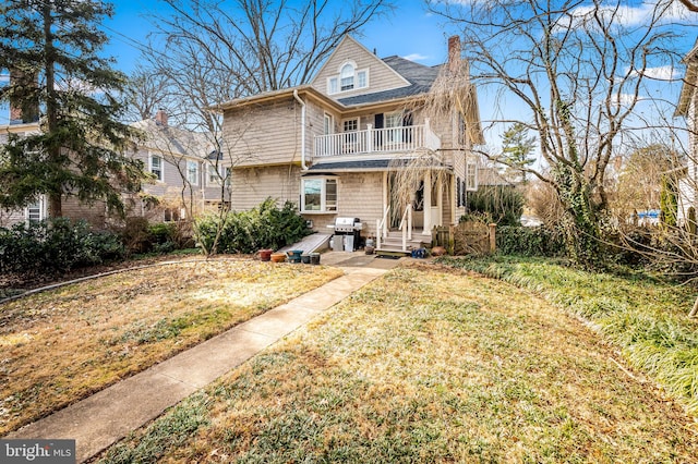 view of front of home featuring entry steps, a chimney, a balcony, and a front yard