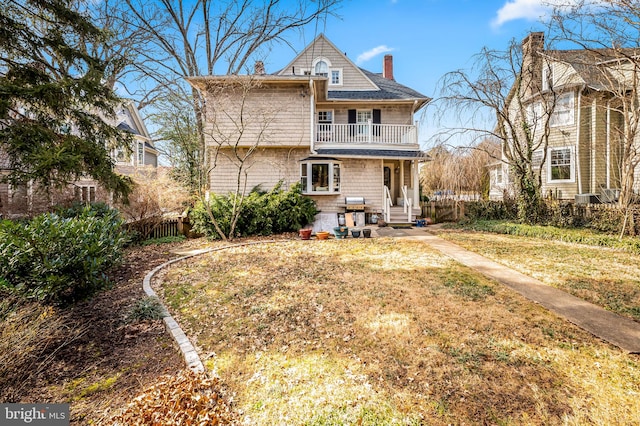 back of property featuring a chimney, fence, a balcony, and a lawn