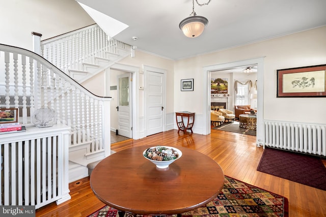 living room featuring a lit fireplace, wood-type flooring, stairway, and radiator heating unit