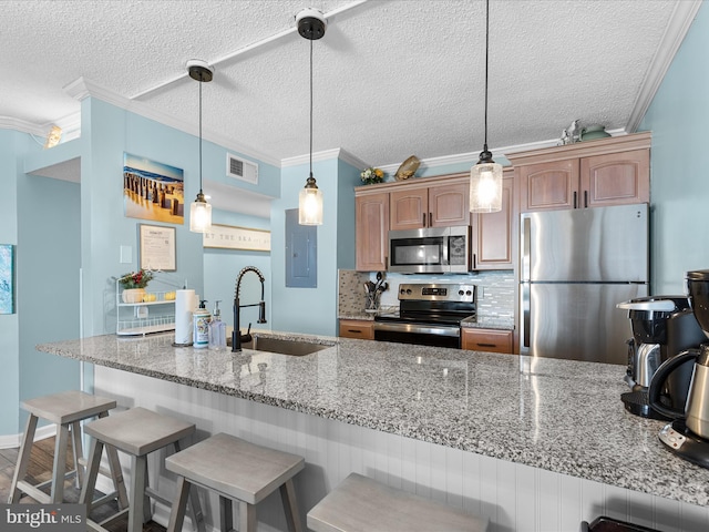 kitchen featuring a kitchen bar, stainless steel appliances, a sink, and decorative light fixtures