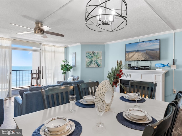 dining space featuring a glass covered fireplace, wood finished floors, a water view, a textured ceiling, and crown molding