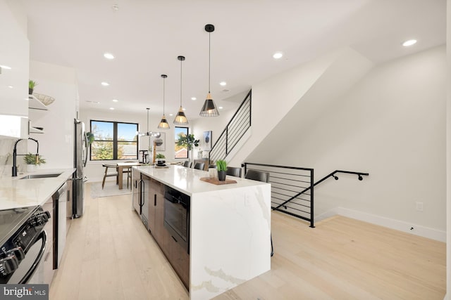 kitchen with light stone counters, decorative light fixtures, a large island, a sink, and black appliances