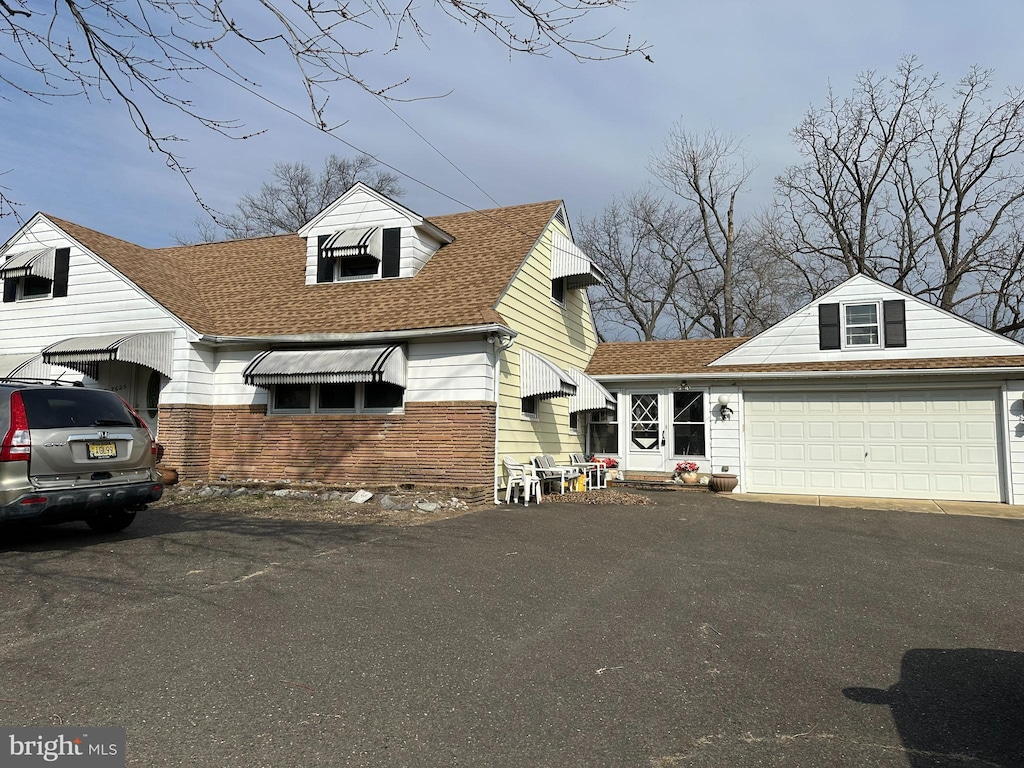 cape cod-style house with aphalt driveway, roof with shingles, and an attached garage