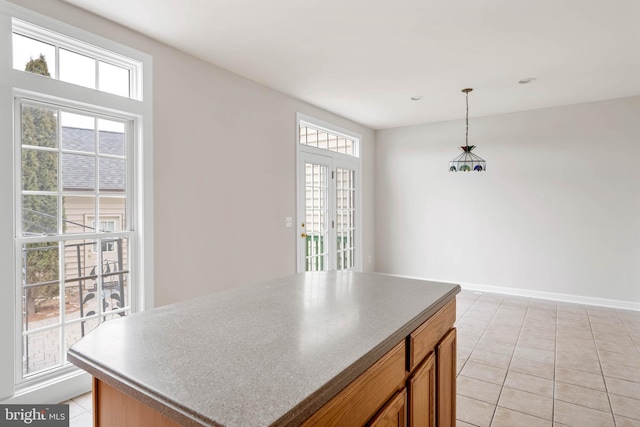 kitchen featuring a center island, hanging light fixtures, brown cabinetry, light tile patterned flooring, and baseboards