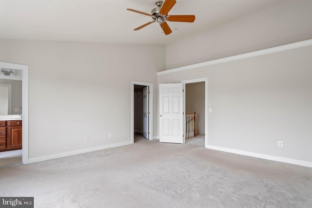 unfurnished bedroom featuring a spacious closet, light carpet, vaulted ceiling, connected bathroom, and baseboards