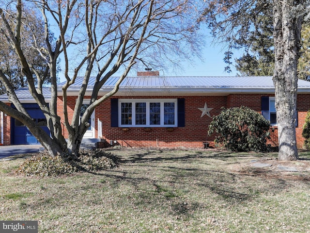 view of front of property with brick siding, a chimney, a front yard, metal roof, and a garage