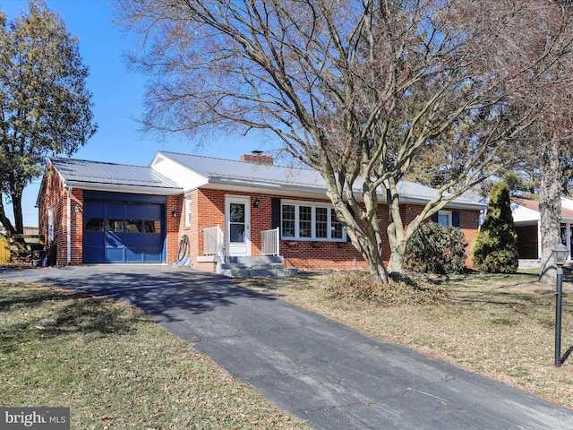 ranch-style house with brick siding, a chimney, metal roof, a garage, and driveway