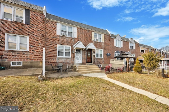 view of property featuring a patio, brick siding, fence, a residential view, and a front lawn