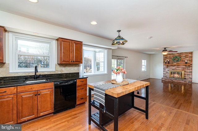 kitchen with light wood finished floors, tasteful backsplash, a brick fireplace, a sink, and dishwasher