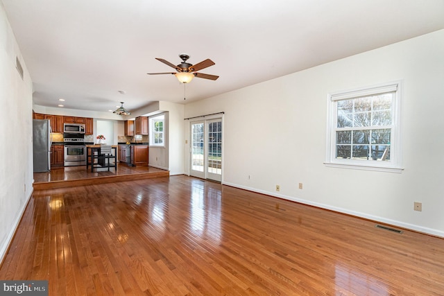 unfurnished living room with a ceiling fan, wood-type flooring, visible vents, and baseboards