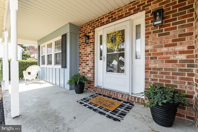 doorway to property featuring covered porch, board and batten siding, and brick siding