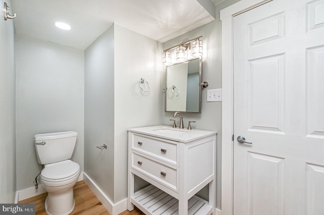 bathroom featuring toilet, baseboards, wood finished floors, and vanity