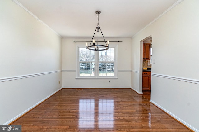 unfurnished dining area with crown molding, a notable chandelier, baseboards, and wood finished floors