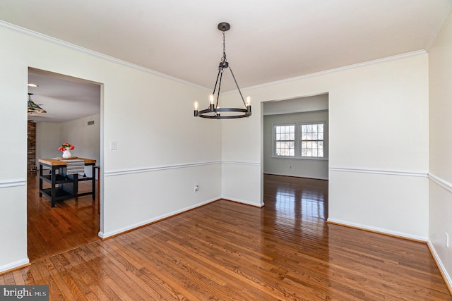 spare room featuring a chandelier, wood-type flooring, ornamental molding, and baseboards