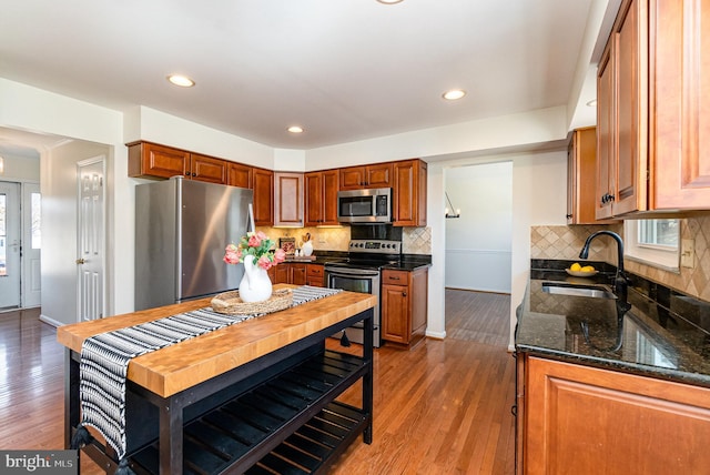 kitchen featuring stainless steel appliances, dark stone counters, a sink, and wood finished floors