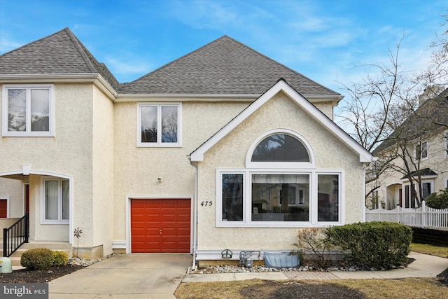 view of front facade featuring a garage, concrete driveway, roof with shingles, and stucco siding