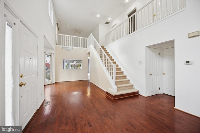 foyer entrance with stairs, visible vents, dark wood finished floors, and a towering ceiling