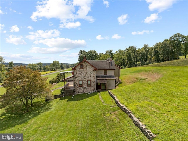 back of property featuring stone siding and a lawn