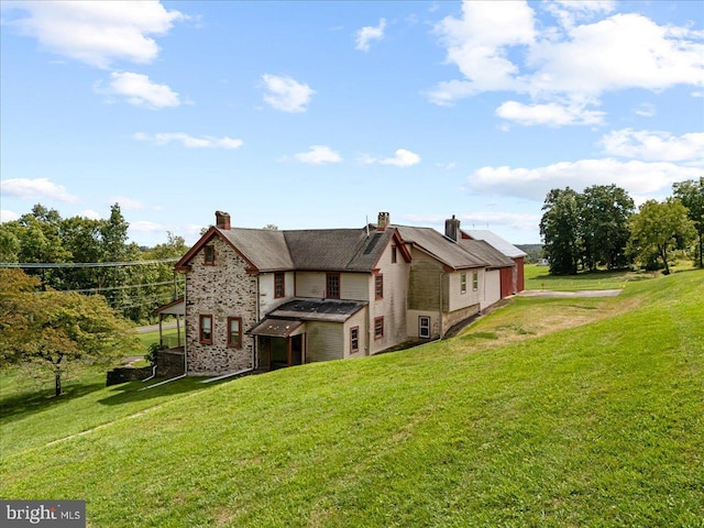 back of house featuring stone siding and a lawn