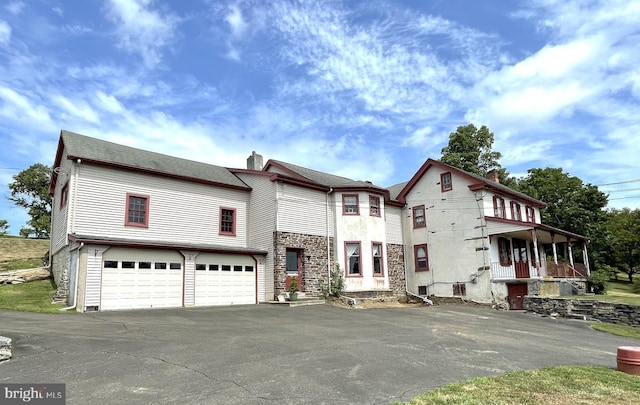 view of front of home with aphalt driveway, roof with shingles, a chimney, an attached garage, and stone siding