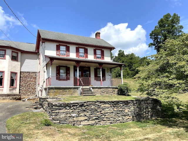 view of front of house with covered porch, a front lawn, a chimney, and stucco siding