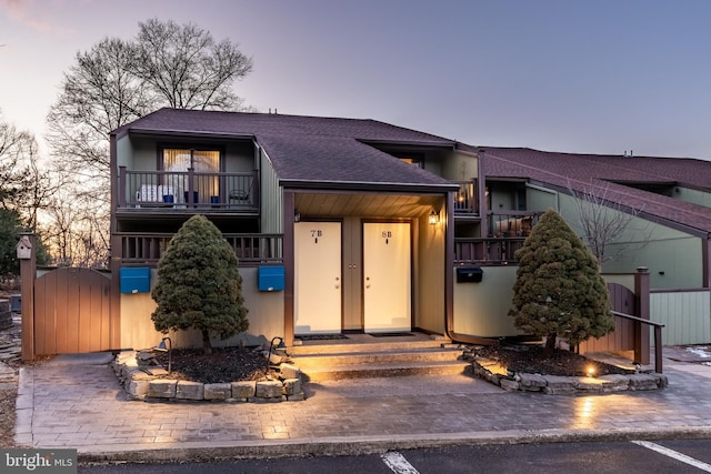 view of front of property with a balcony, a gate, fence, and roof with shingles