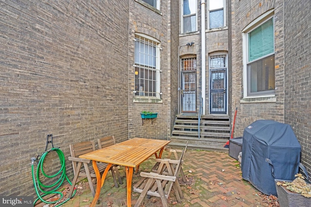 view of exterior entry featuring outdoor dining space, brick siding, and a patio