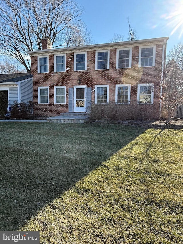 colonial house featuring brick siding, a chimney, and a front yard