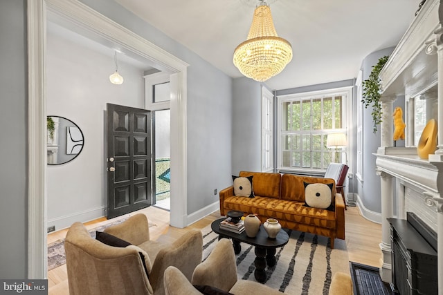 living room with a chandelier, baseboards, a fireplace, and light wood-style floors