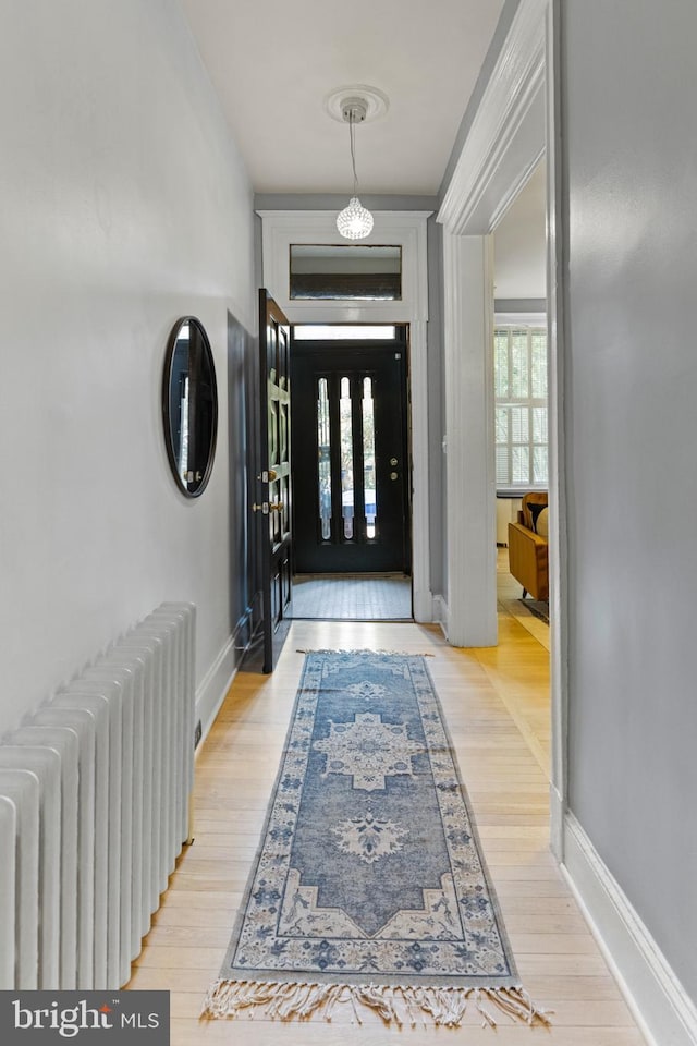 foyer entrance with light wood-style floors, radiator heating unit, and baseboards