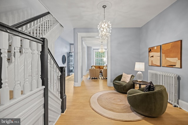 sitting room featuring a notable chandelier, radiator heating unit, wood finished floors, baseboards, and stairs