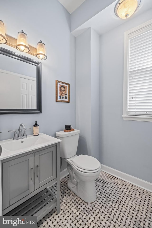 half bath with tile patterned flooring, baseboards, vanity, and toilet