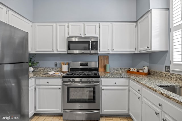 kitchen with light stone countertops, appliances with stainless steel finishes, and white cabinets