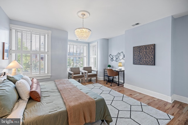 bedroom with light wood-style floors, a chandelier, visible vents, and baseboards