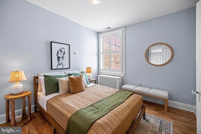 bedroom featuring baseboards, visible vents, radiator heating unit, and wood finished floors