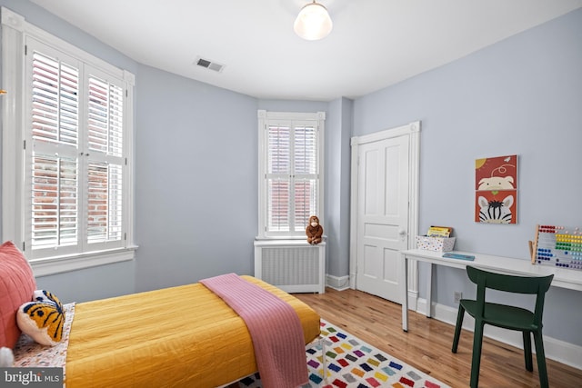 bedroom featuring light wood-style floors, radiator, visible vents, and baseboards