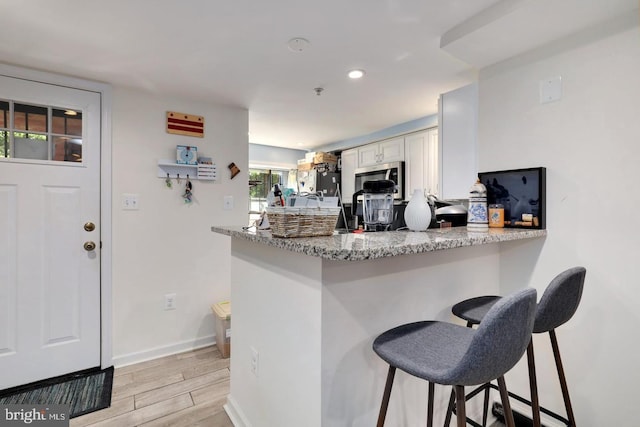 kitchen featuring white cabinetry, stainless steel microwave, a peninsula, and light stone countertops