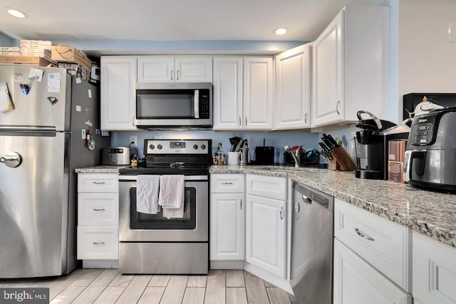 kitchen with white cabinets, appliances with stainless steel finishes, light stone countertops, wood tiled floor, and a sink