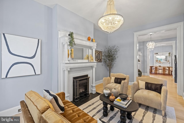 living room featuring a fireplace with flush hearth, baseboards, a notable chandelier, and wood finished floors