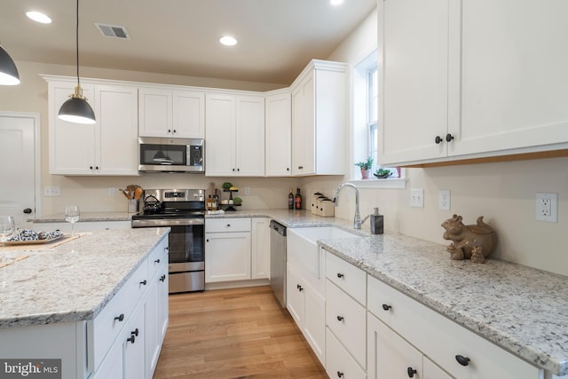 kitchen with stainless steel appliances, light stone countertops, white cabinets, light hardwood / wood-style floors, and pendant lighting