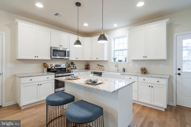 kitchen featuring appliances with stainless steel finishes, hanging light fixtures, light stone countertops, and white cabinets